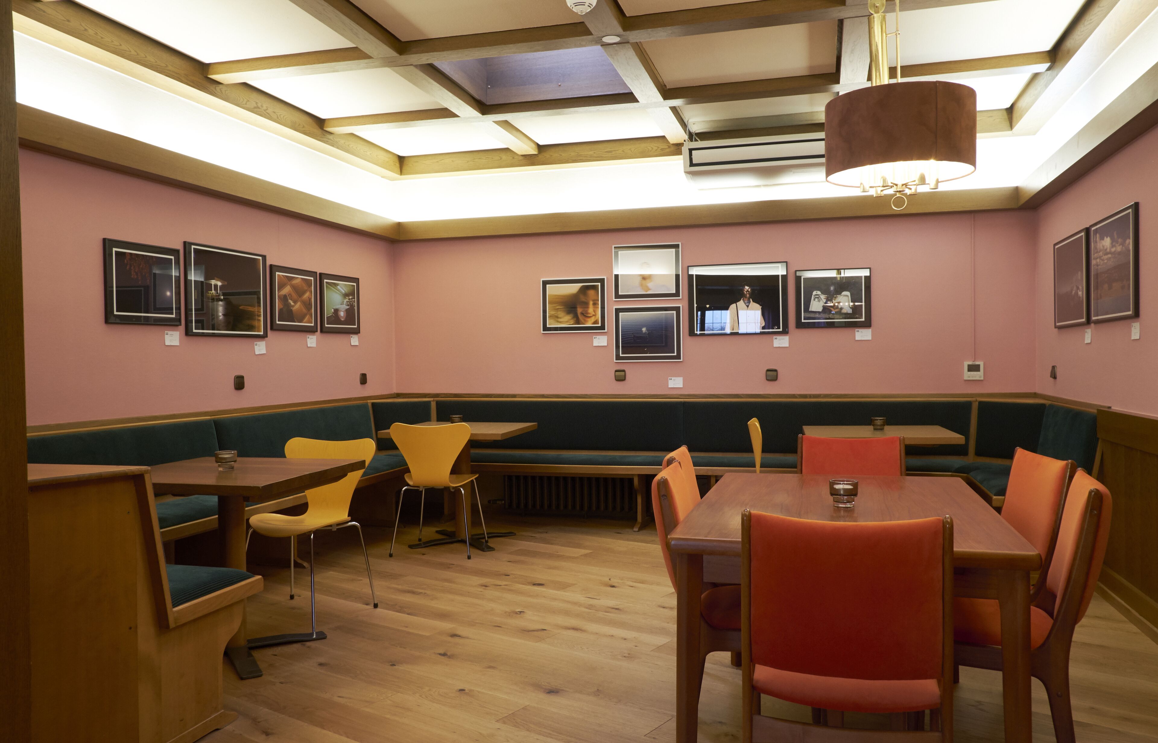 Un restaurante con mesas y sillas de madera, un techo alto con tragaluces y cuadros enmarcados en las paredes.