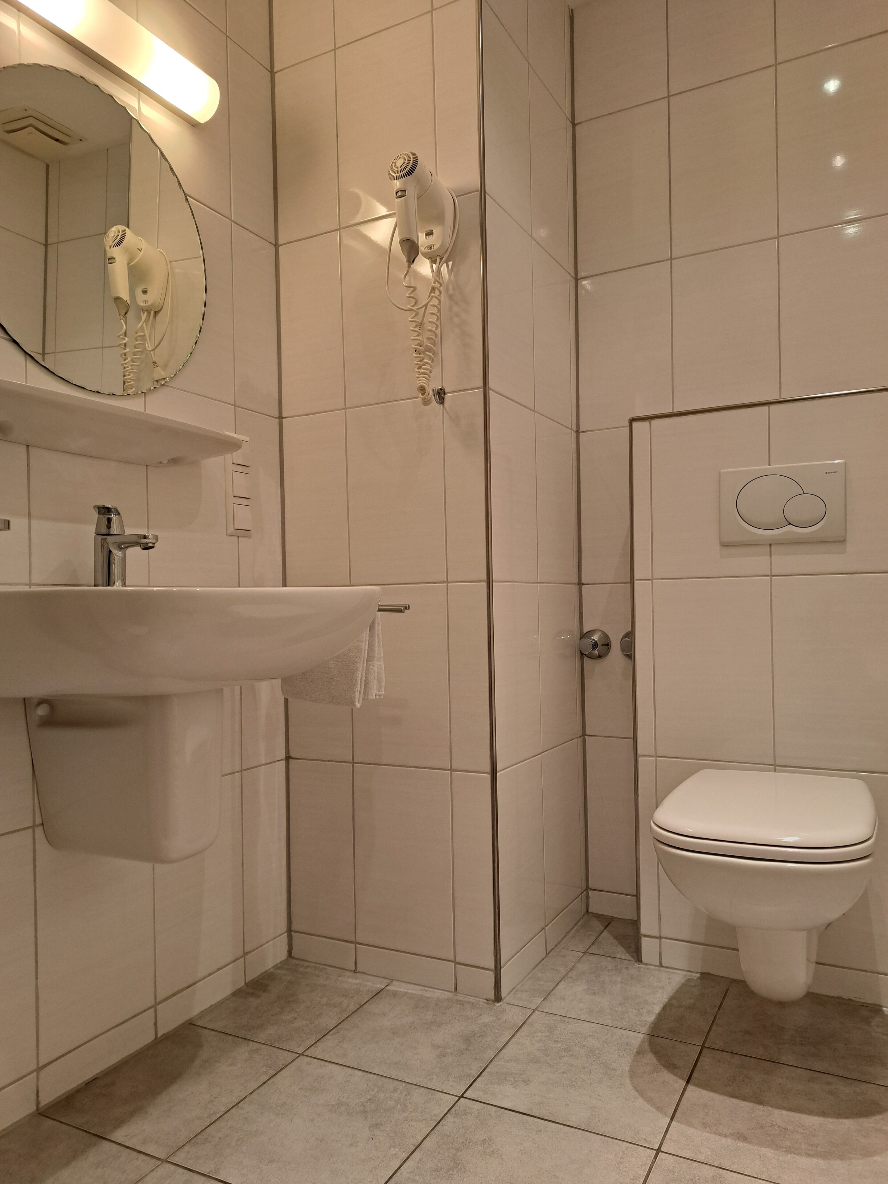 Un baño moderno con lavamanos, espejo, secador de pelo y retrete.