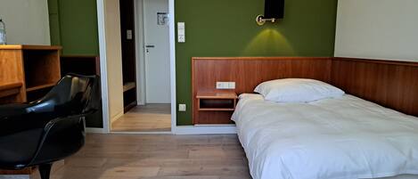 Een kamer met een bed, een stoel, een houten nachtkastje en een groene wand met een wandlamp.