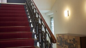 Eine Treppe mit roten Teppichstufen, einem hölzernen Geländer und einer wandmontierten Leuchte.