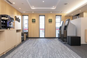 En modern hotellobby med heltäckningsmatta på golvet, väggar beklädda med träpaneler och en receptionsdisk med en kaffemaskin.