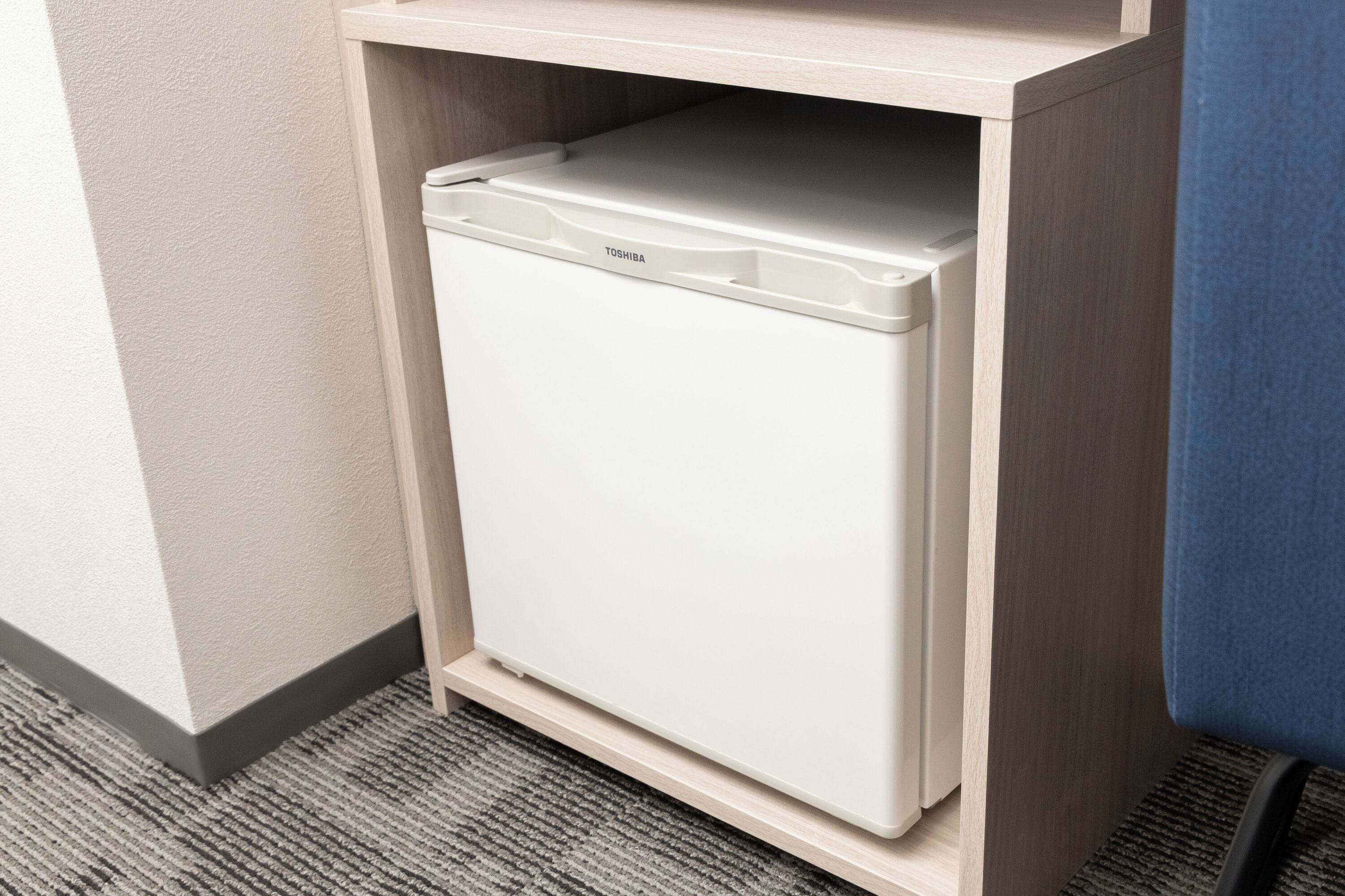 A white refrigerator in a kitchen cabinet with a light wood finish.