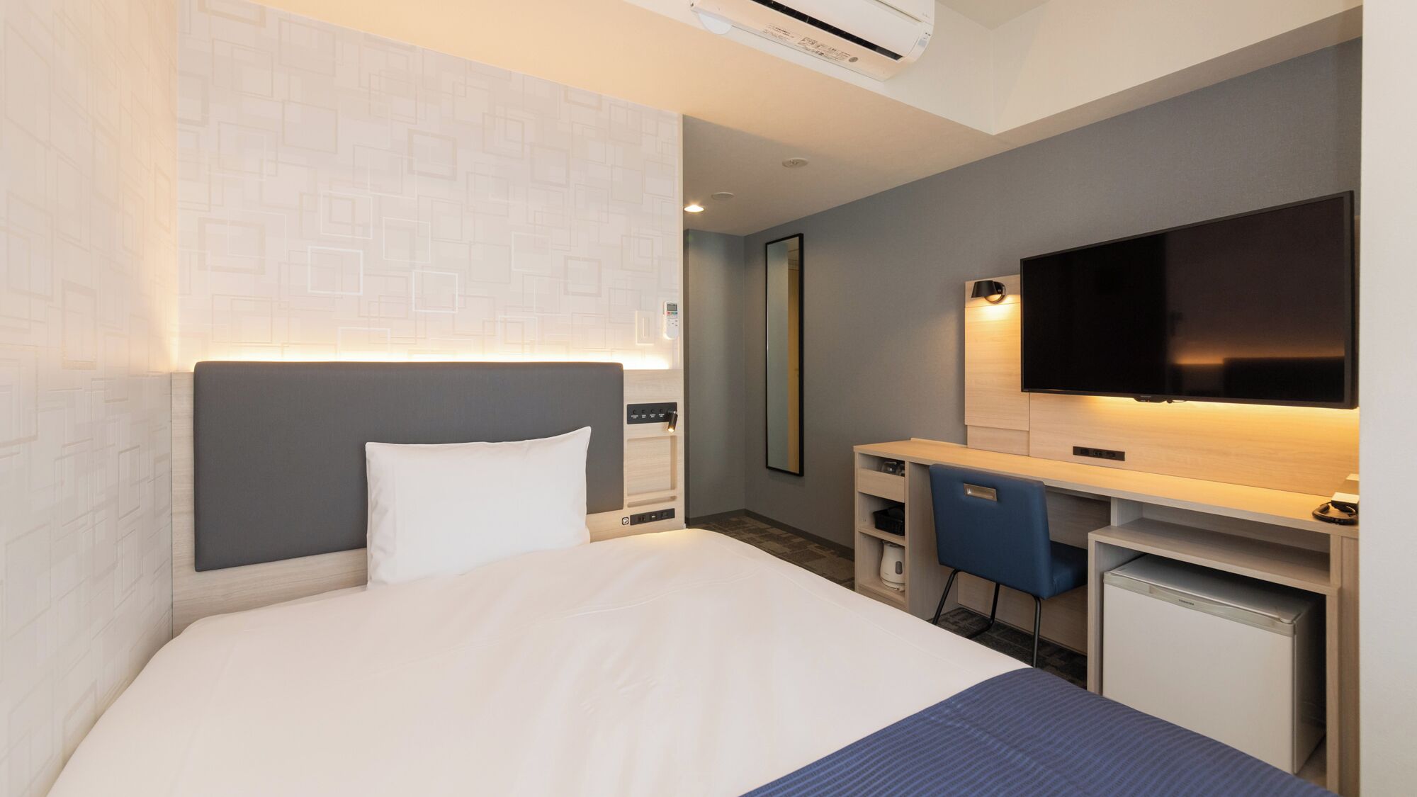 Une chambre d’hôtel équipée d’un lit, d’un bureau, d’une chaise, d’une télévision et d’un miroir.