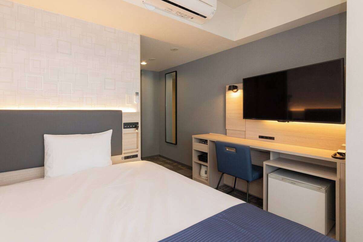 A hotel room with a bed, desk, chair, TV, and a mirror.