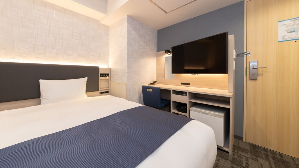 Une chambre d’hôtel comprenant un lit, un bureau avec un téléviseur à écran plat, un miroir et une armoire.