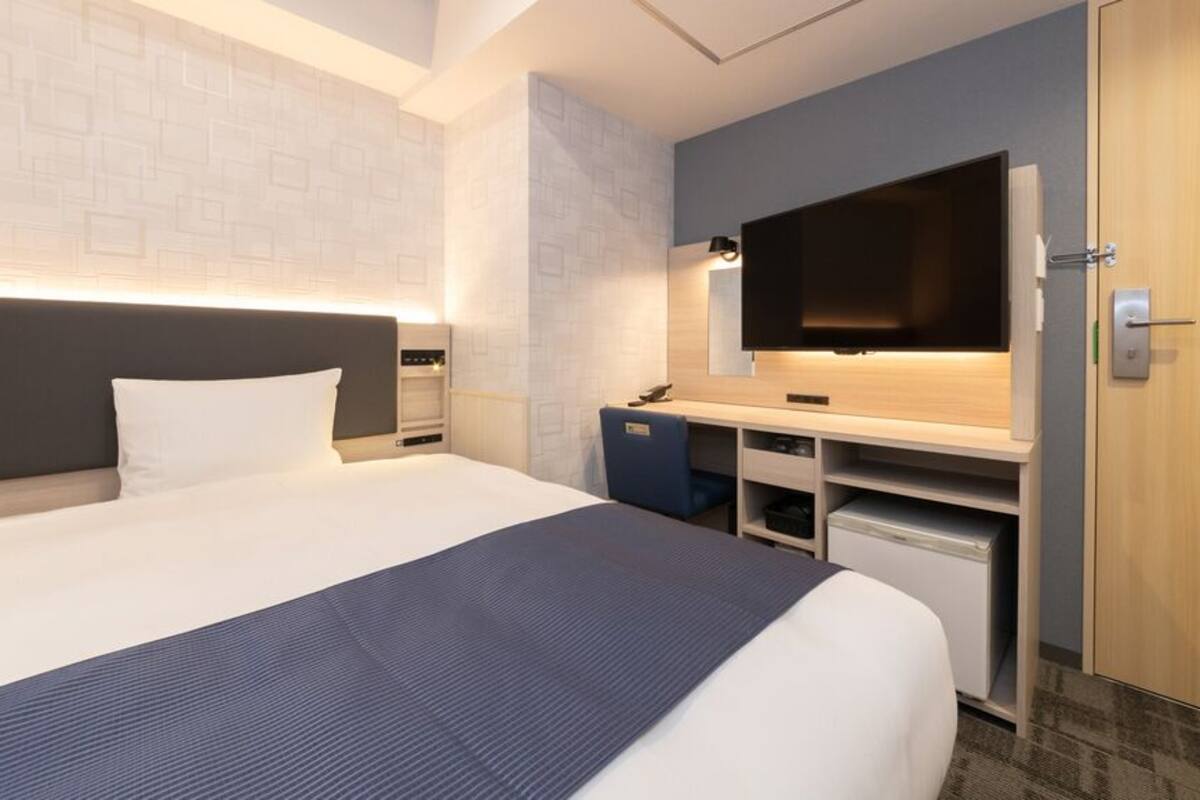 A hotel room with a bed, a desk with a flat-screen TV, a mirror, and a wardrobe.