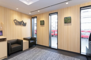 Een modern receptiegebied met een houten wand, twee zwarte leren banken, een vloerbedekking en een glazen deur naar buiten.