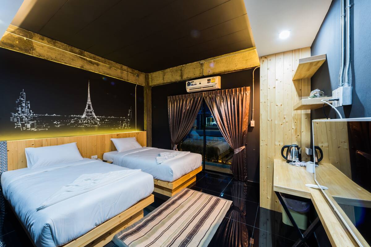 Une chambre d’hôtel avec deux lits, un bureau, une machine à café et une fresque représentant un paysage urbain sur le mur.