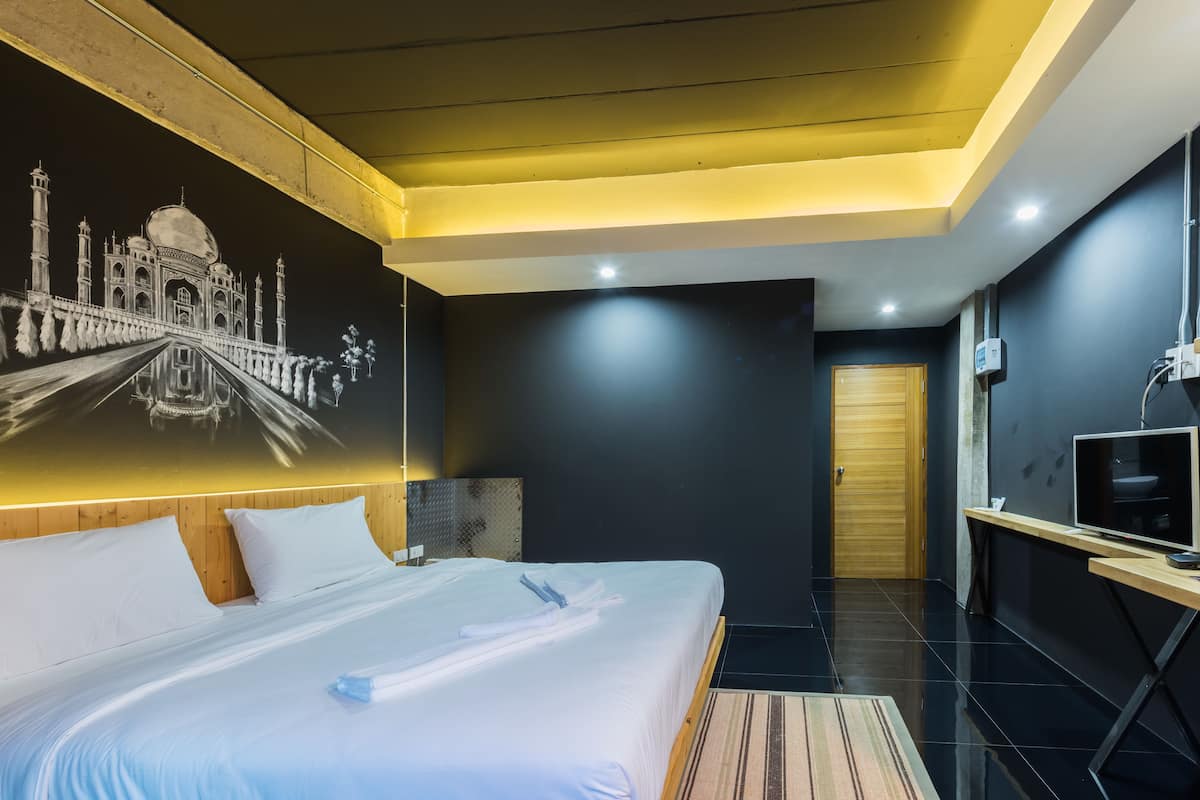 Une chambre d’hôtel avec un grand lit, un bureau, une télévision et une fresque murale représentant le Taj Mahal.