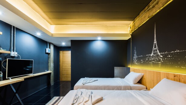 A hotel room with two beds, a desk with a flat-screen TV, a wall-mounted picture of the Eiffel Tower, and a wooden ceiling. - Nine Blue Residence (Pattaya)