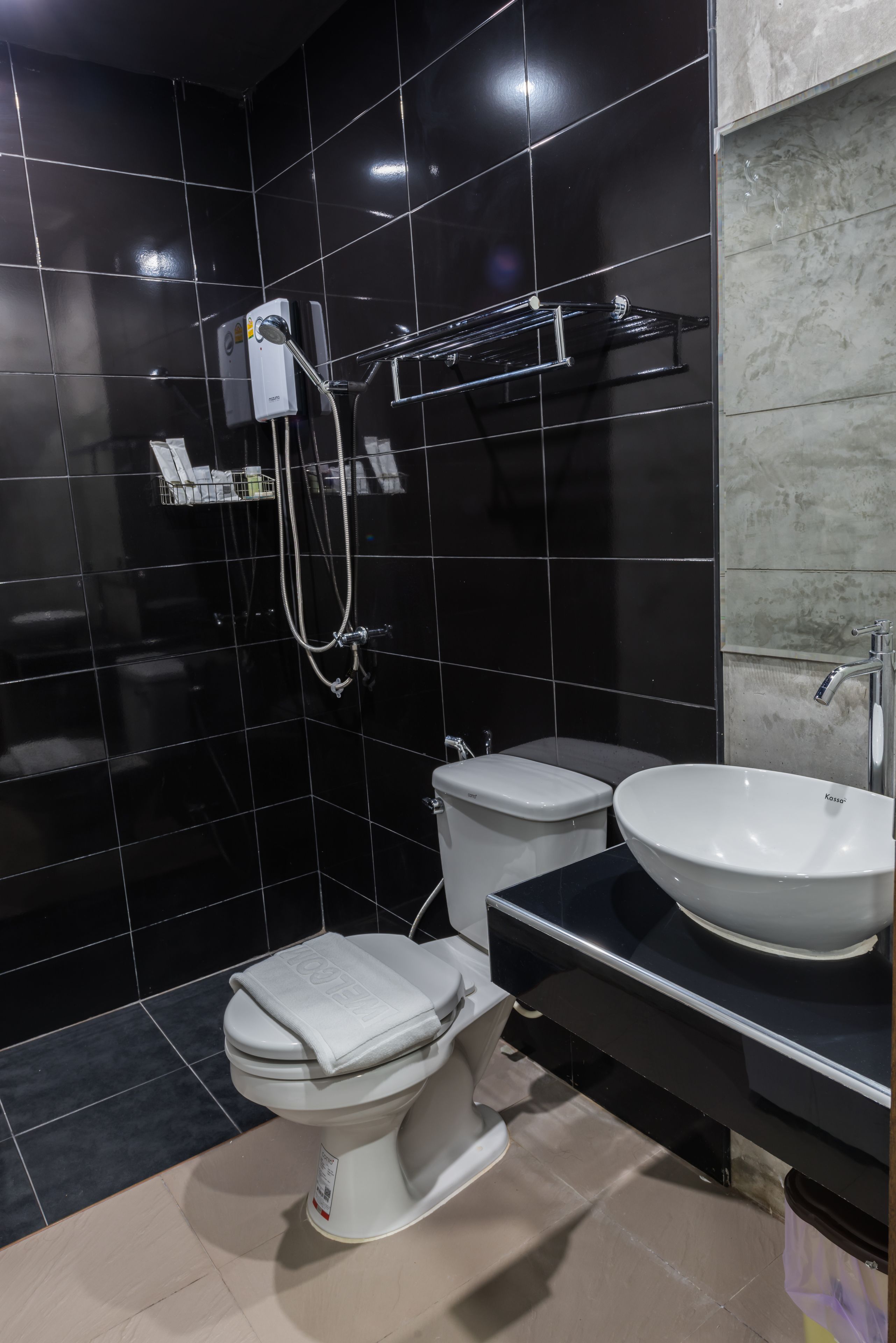 A modern bathroom with black tiled walls, a white toilet, a bidet, a sink, and a showerhead.