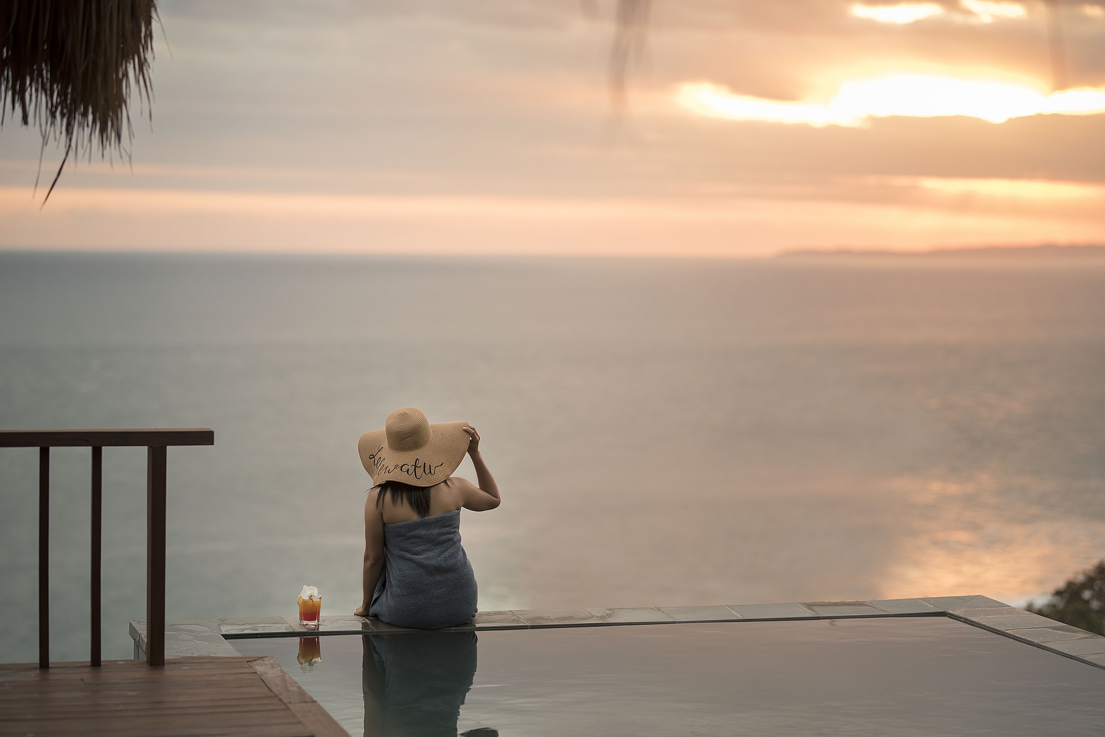 A person sitting on a glass infinity pool with a sunset view.