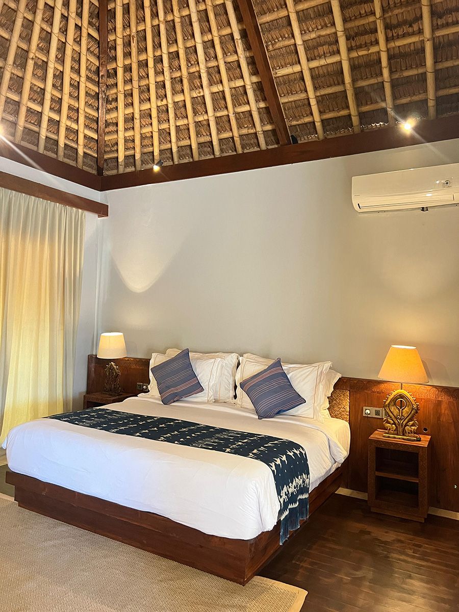 A hotel room with a large bed, wooden headboard, a ceiling fan, and a nightstand with a lamp.