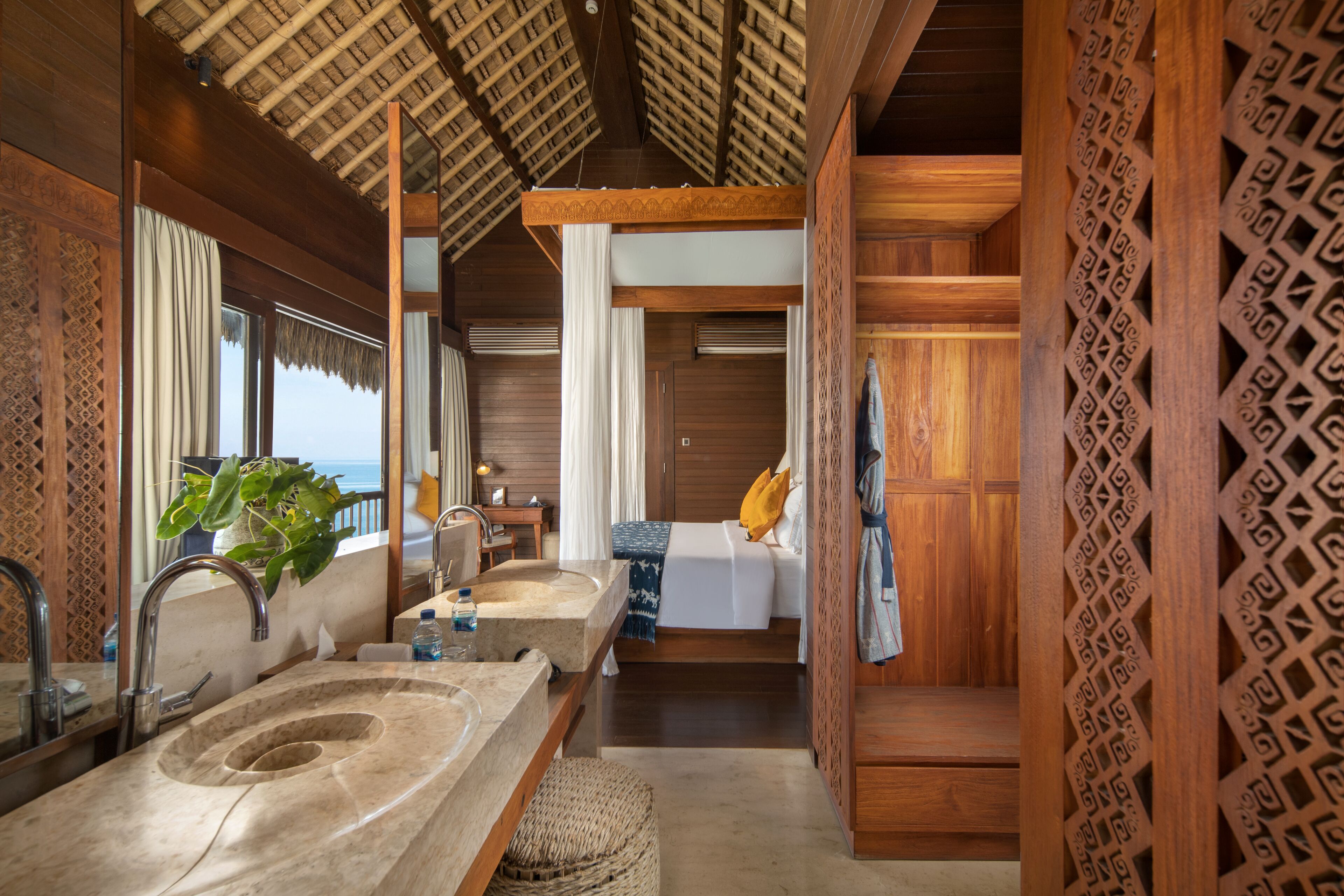 A room with a large sink, a mirror, a bed with a pillow, and a view of the ocean.
