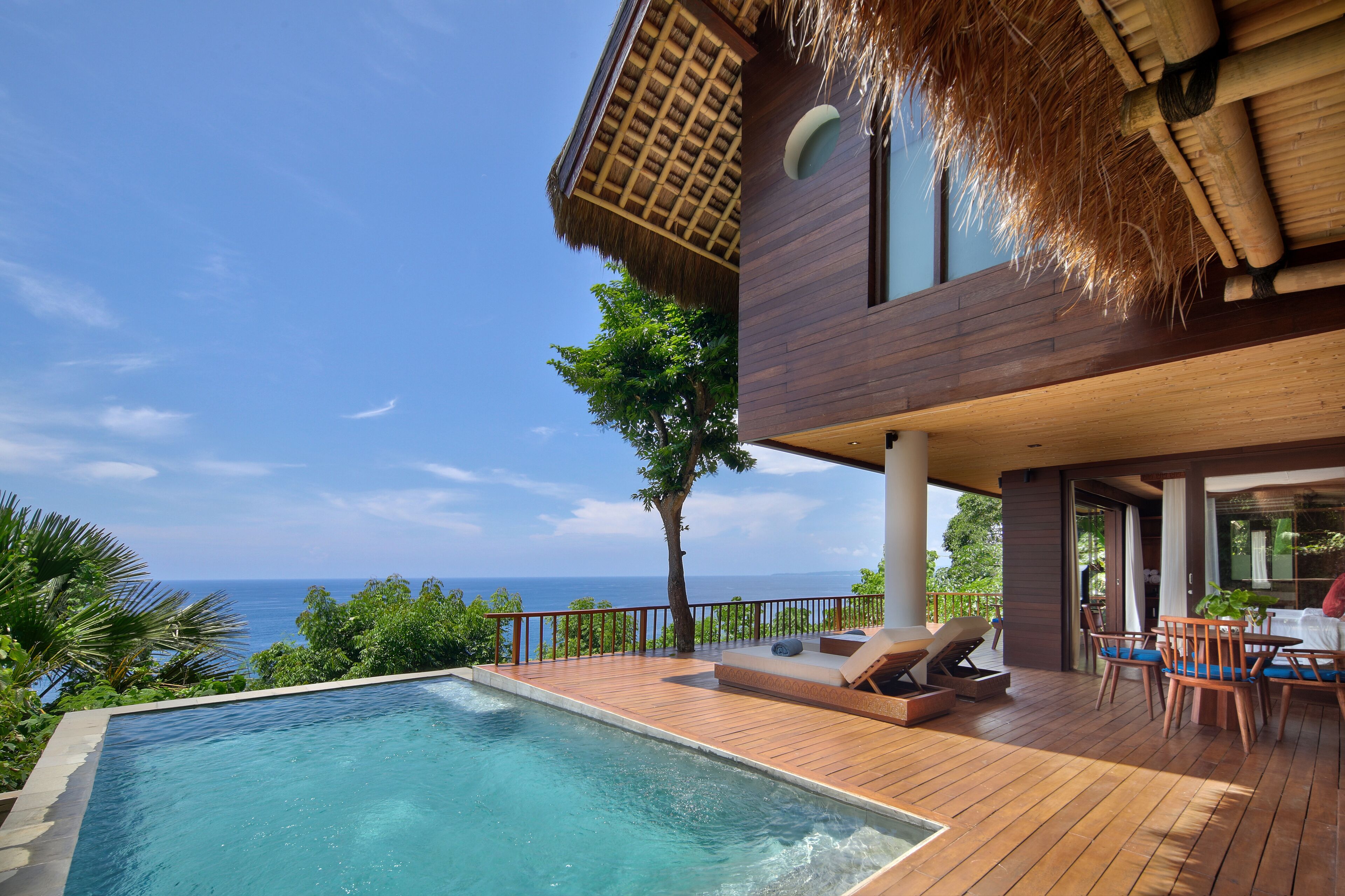 Una villa moderna con terraza de madera, piscina y vistas al océano.