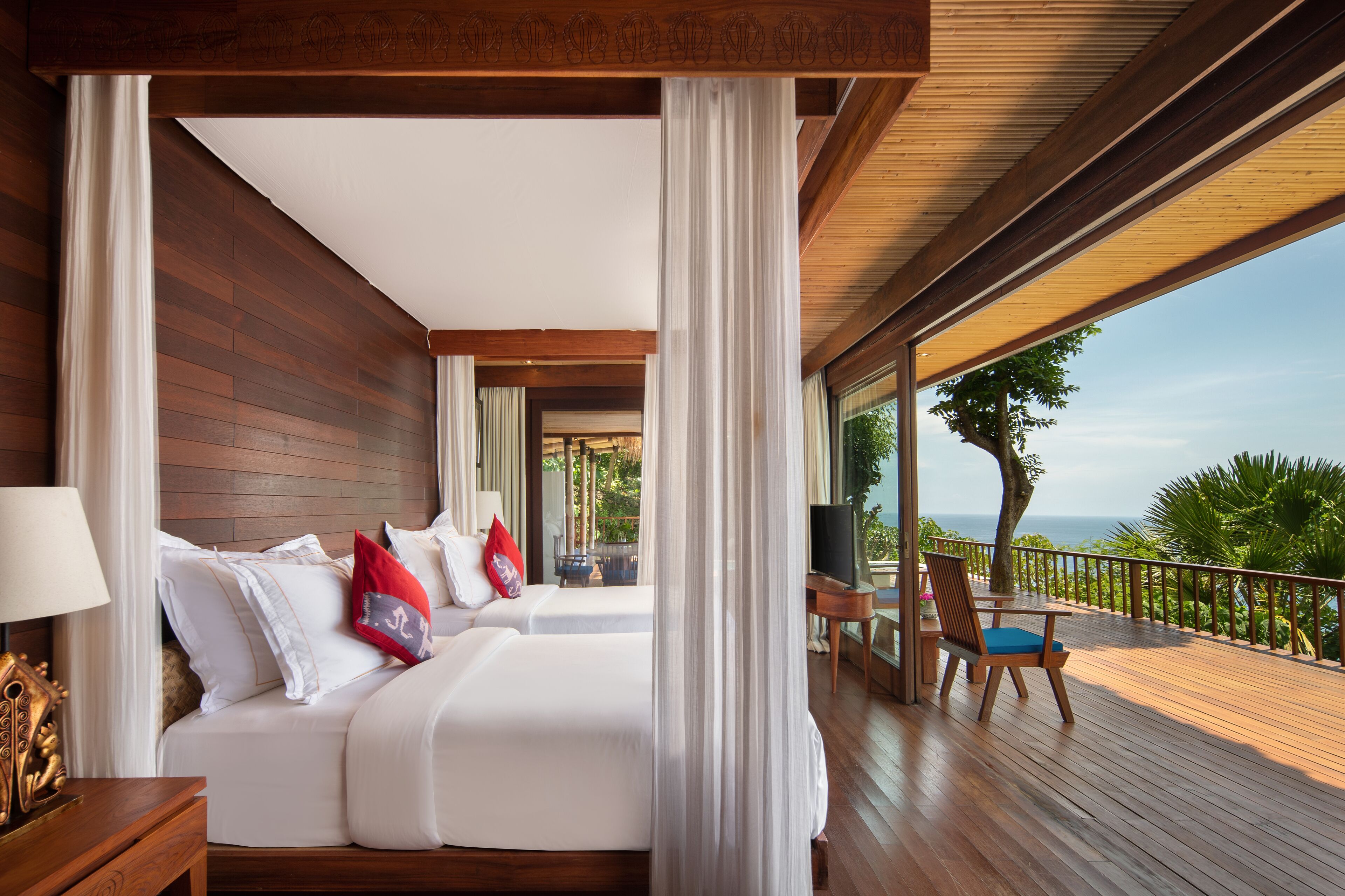 A hotel room with two beds, a balcony with a view of the ocean, and a wooden deck.