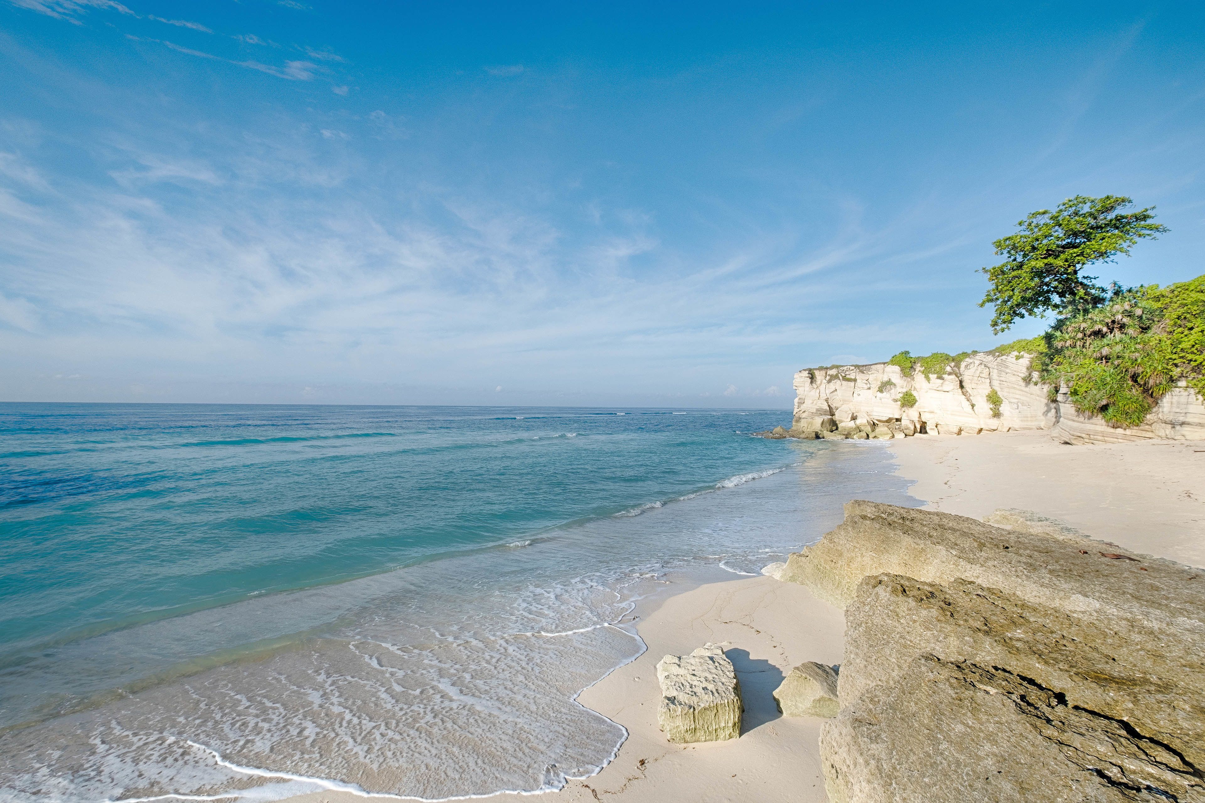 Une plage à l’eau d’un bleu limpide, avec un rivage sablonneux et des falaises rocheuses.