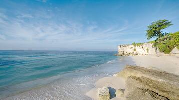 Une plage à l’eau d’un bleu limpide, avec un rivage sablonneux et des falaises rocheuses.