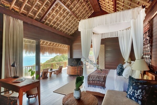 A room with a bed, a TV, a desk, and a view of the ocean.