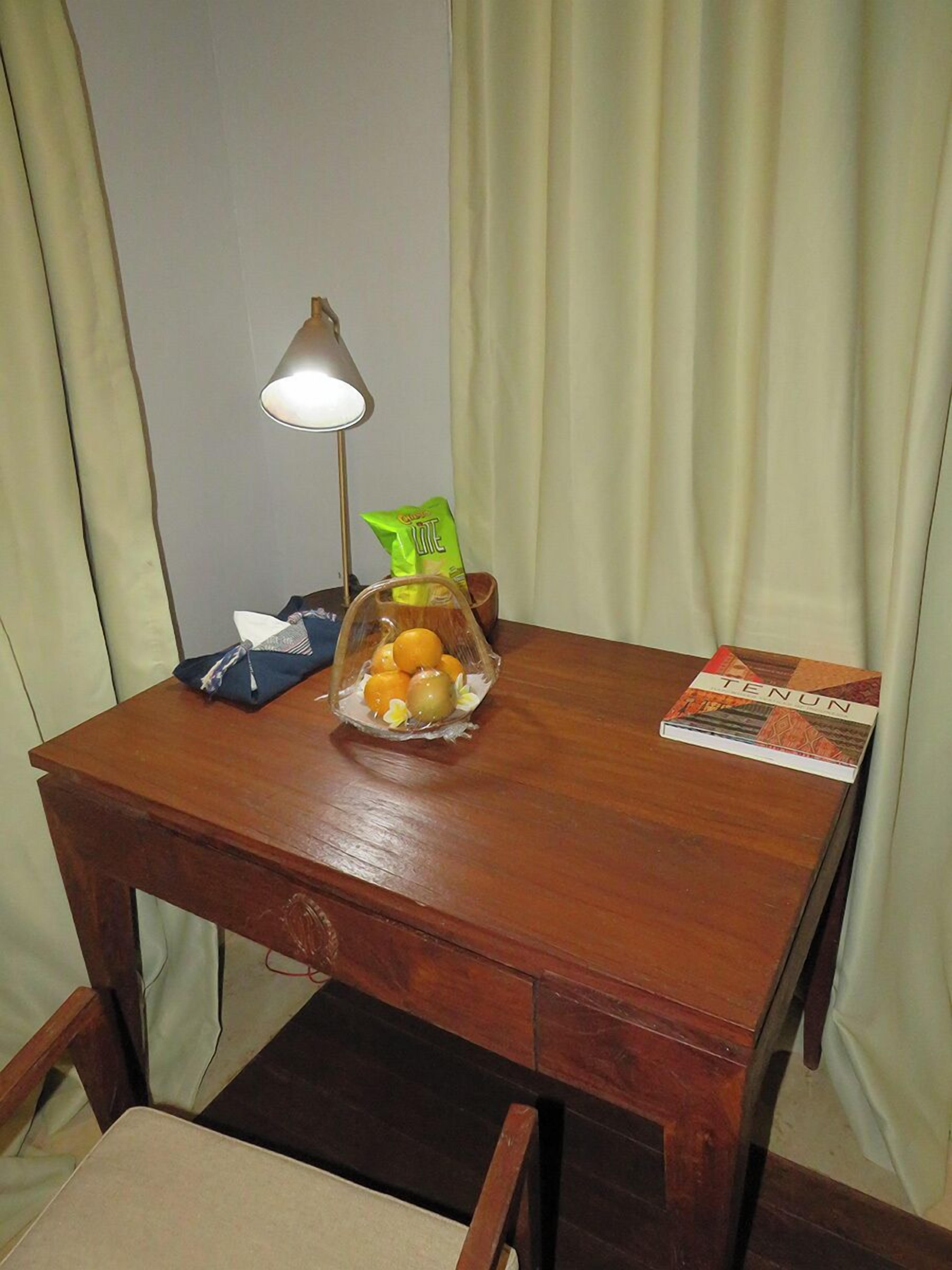 Un escritorio de madera con una lámpara, un frutero, una caja de pañuelos y un libro titulado 'TENUN'.