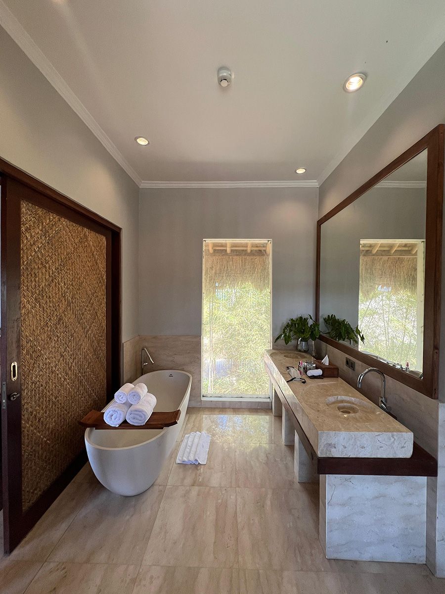 A modern bathroom with a freestanding bathtub, a large mirror, and a window with a view of greenery.