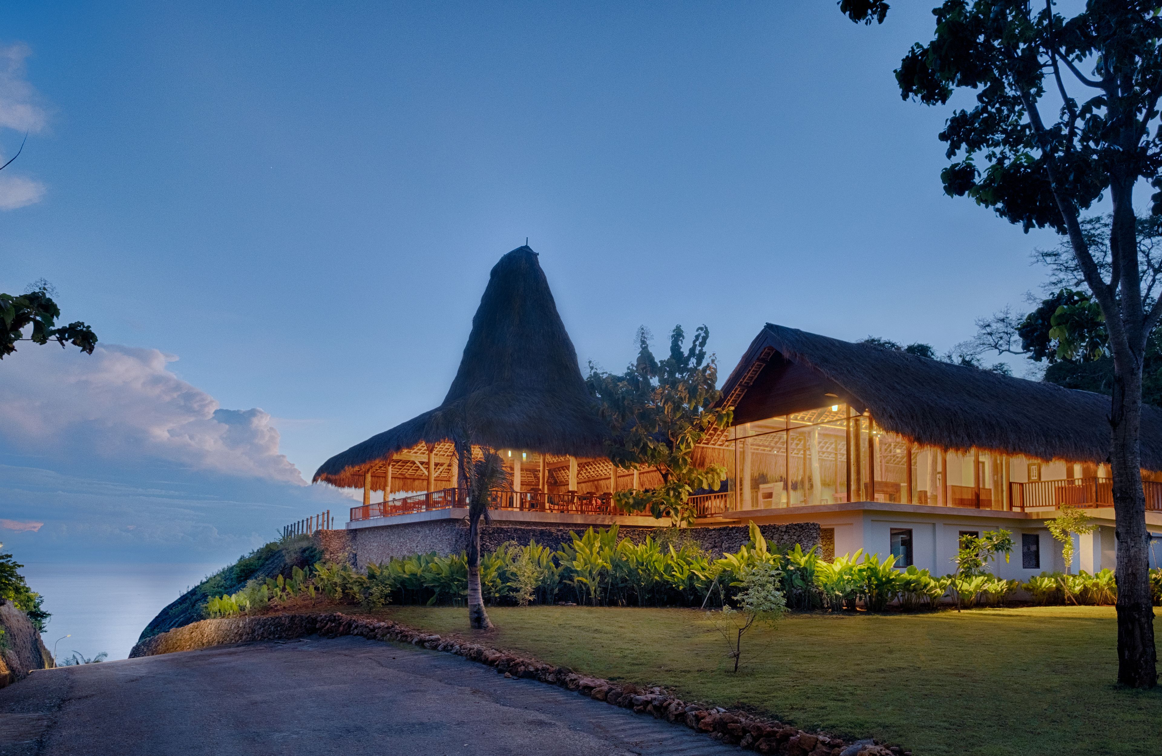 A resort with a thatched-roof building, a large tree, and a view of the ocean.