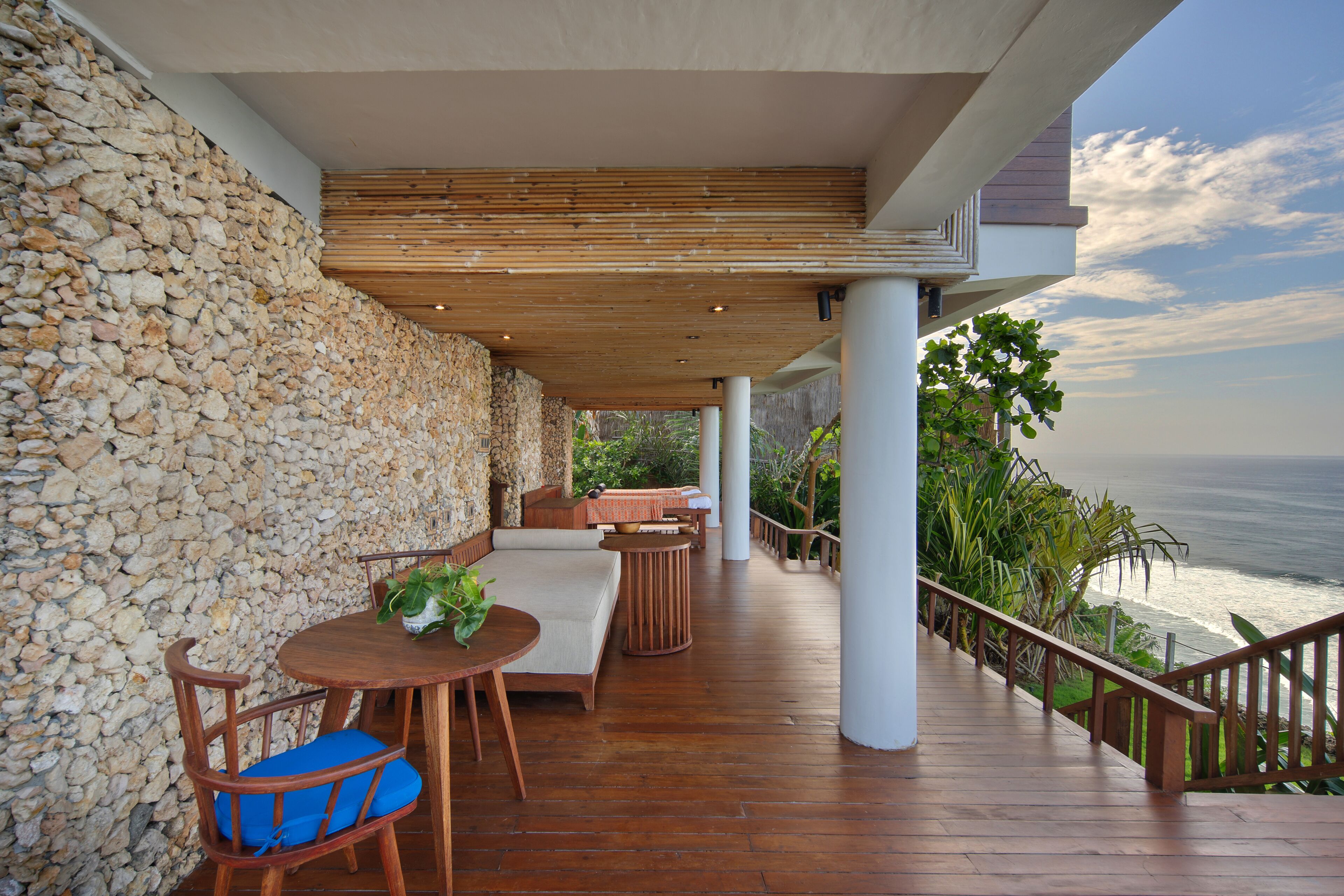 Una terraza de madera con mobiliario exterior, un muro de piedra y vista al océano.