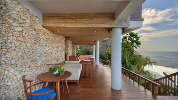 Una terraza de madera con mobiliario exterior, un muro de piedra y vista al océano.