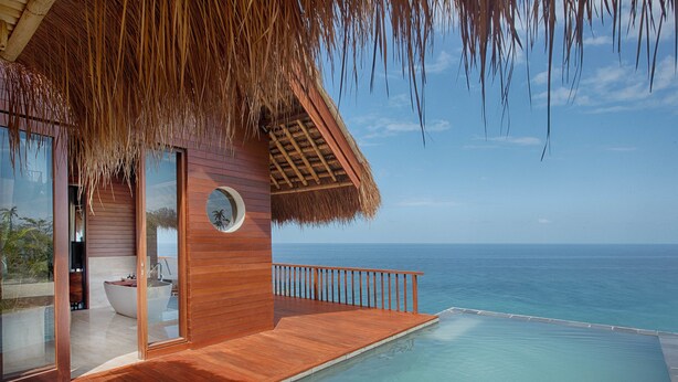 Una villa moderna con terraza de madera, piscina infinita y vistas al océano.