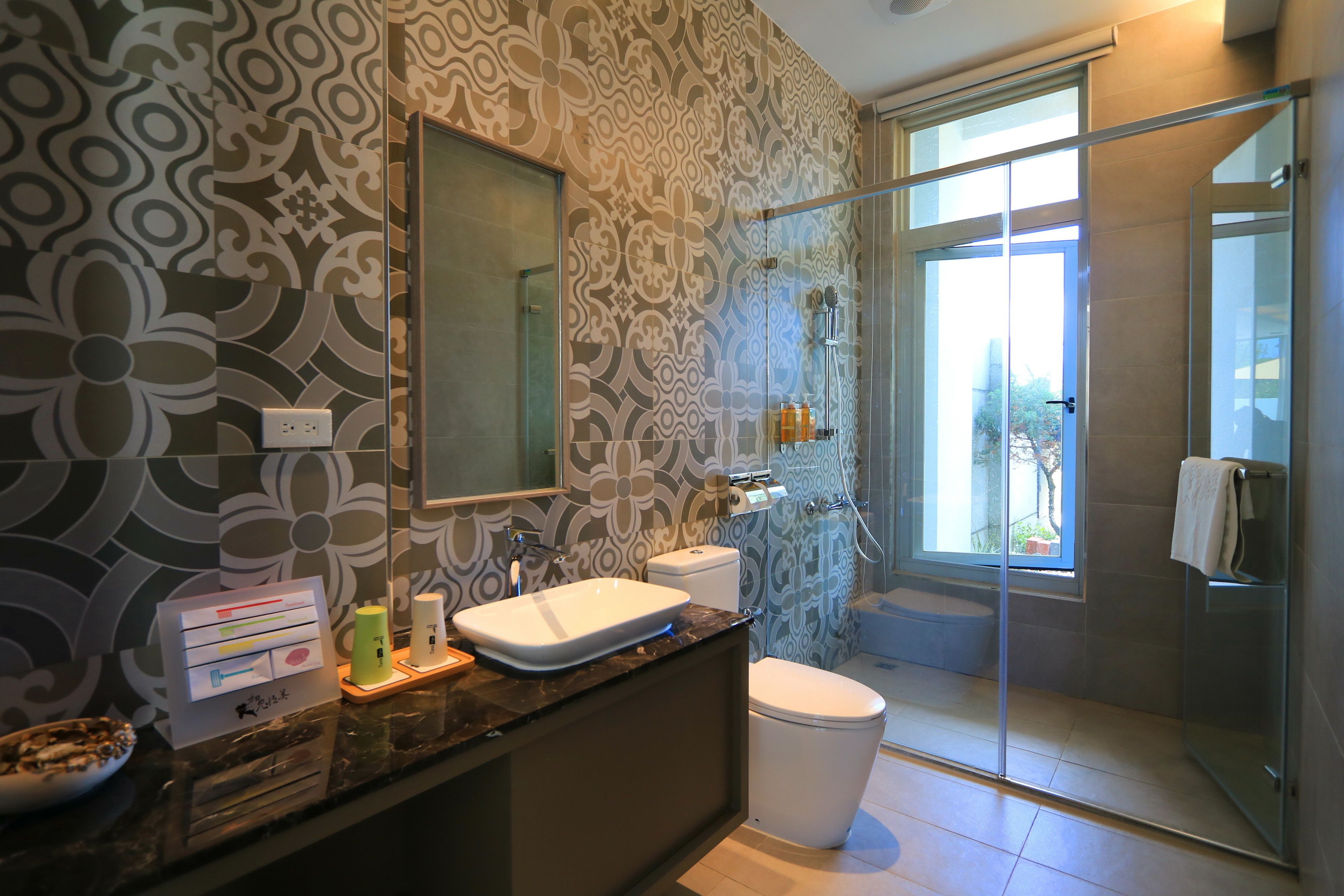 Un baño moderno con un papel tapiz estampado, un espejo grande, un lavamanos, un inodoro y un box de ducha de cristal.