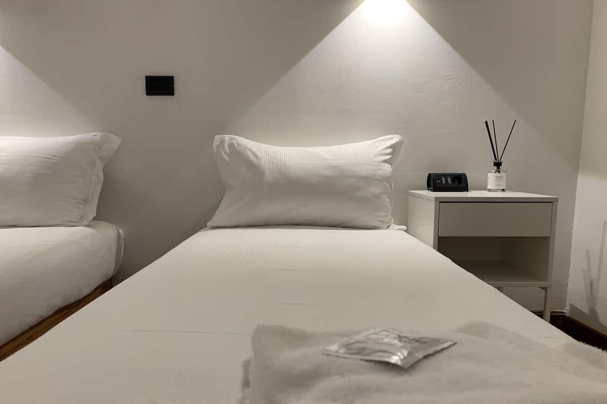 A hotel room with a single bed, a bedside table with a lamp and a bottle of air freshener, and a nightstand with a drawer.