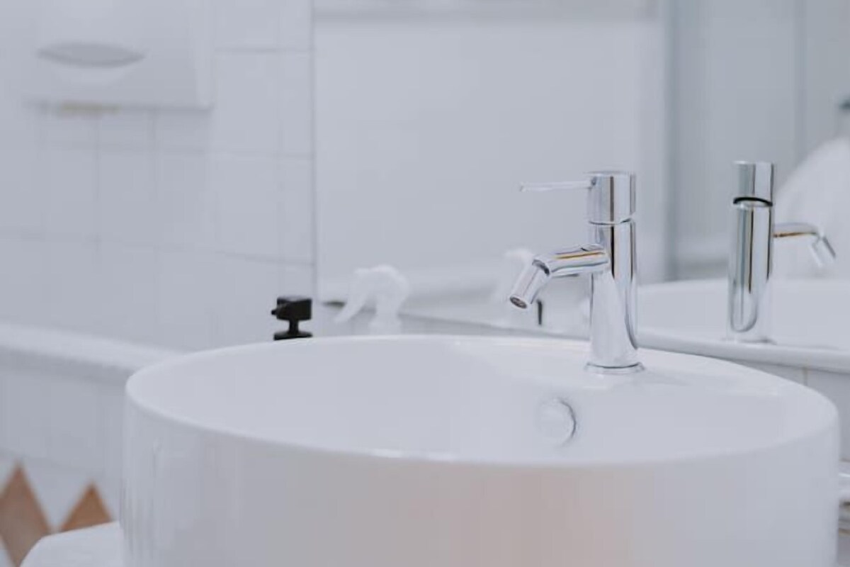 A bathroom with a round white sink, a wooden vanity, and a white tiled wall.