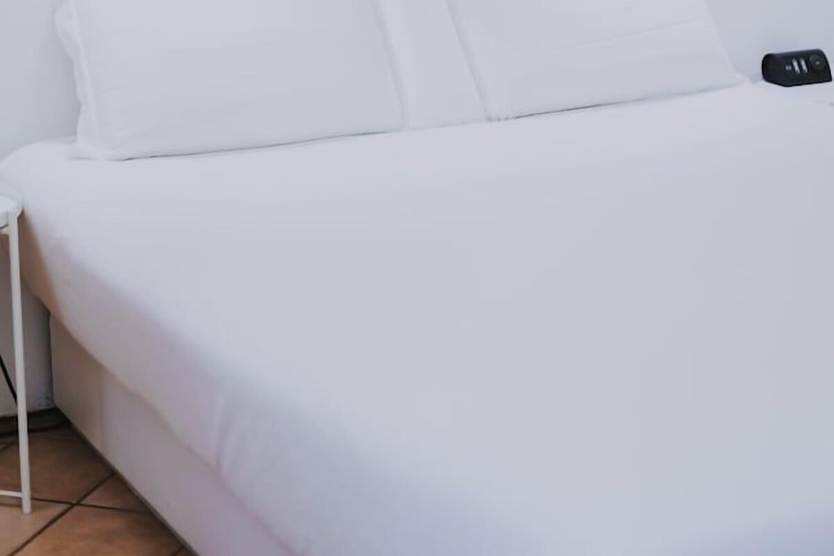 A minimalist hotel room with a bed, white bedding, and a small bedside table.