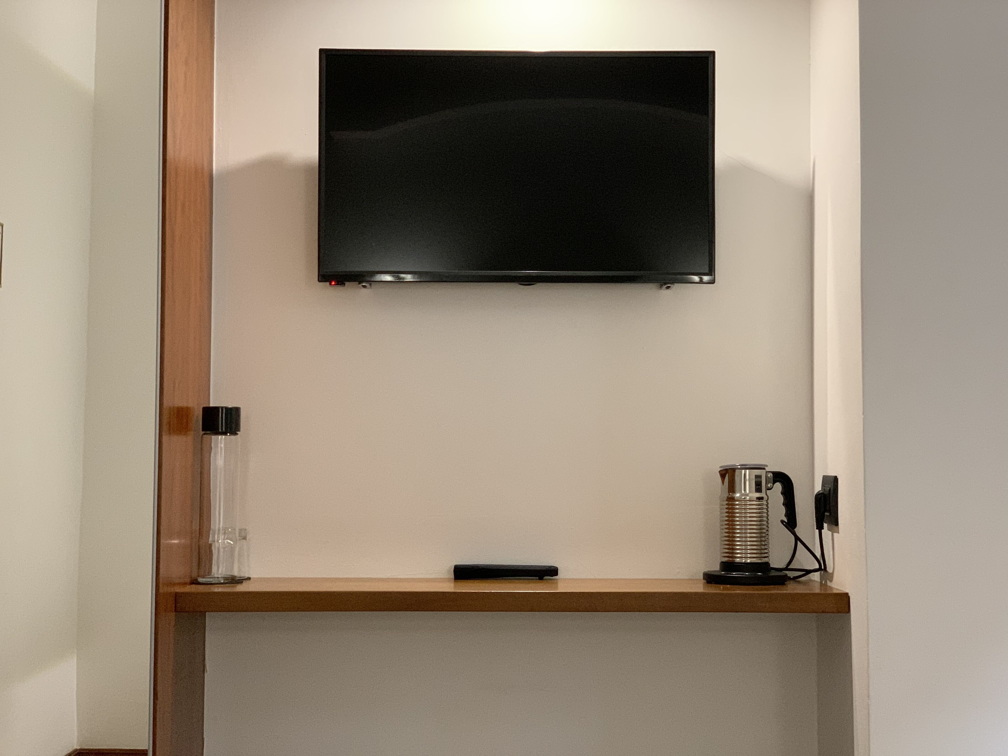 A flat-screen TV mounted on a wall above a wooden shelf.