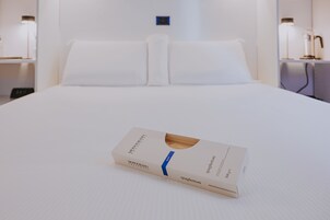A neatly made bed with a box of Monograno Spaghetti on it.