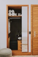 A wooden wardrobe with a mirror, a small black stool, and neatly rolled towels.