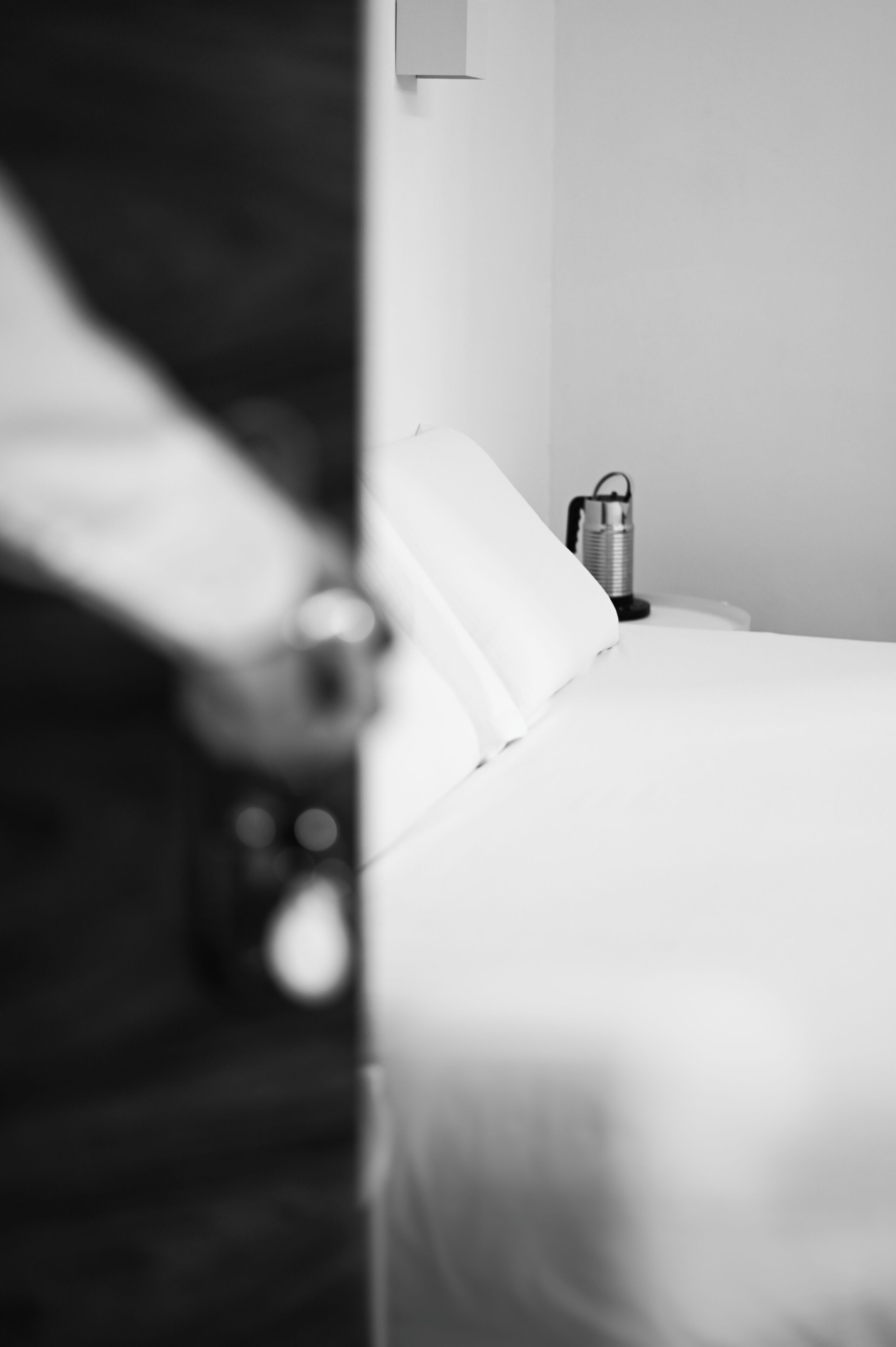 Una habitació d'hotel amb un llit ben arreglat, una taula de nit amb una làmpada i un llum fixat a la paret.