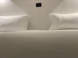 A bed with two pillows and a small black object on the wall.