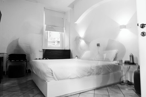 Una habitación de hotel moderna con una cama, una mesita pequeña, una silla y un ventanal.
