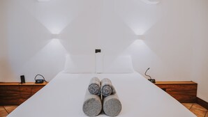 A neatly made bed with rolled towels, a bedside table with a speaker and phone, and a wooden bench along the wall. - Albergo delle Regioni (Rome)