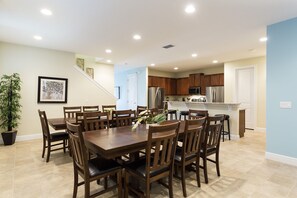 A spacious dining area with a large wooden table and chairs, a kitchen with wooden cabinets and stainless steel appliances, and a potted plant. - The Encore Club #4 - 10 Bed 10 Baths Villa (Kissimmee)