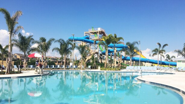 A swimming pool with a water park in the background, palm trees, and lounge chairs. - The Encore Club #4 - 10 Bed 10 Baths Villa (Kissimmee)
