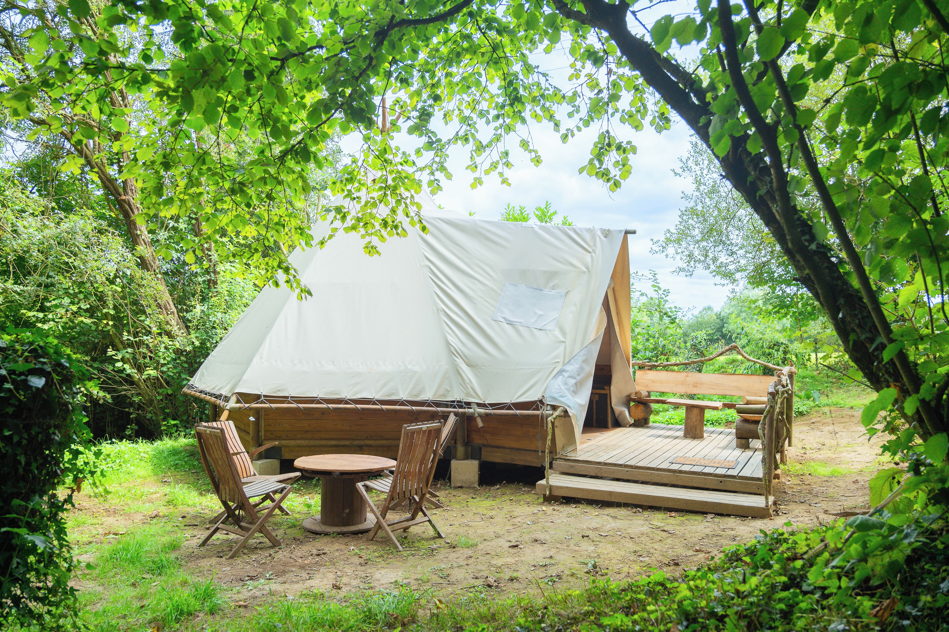 A tent with a picnic table and chairs in a wooded area.