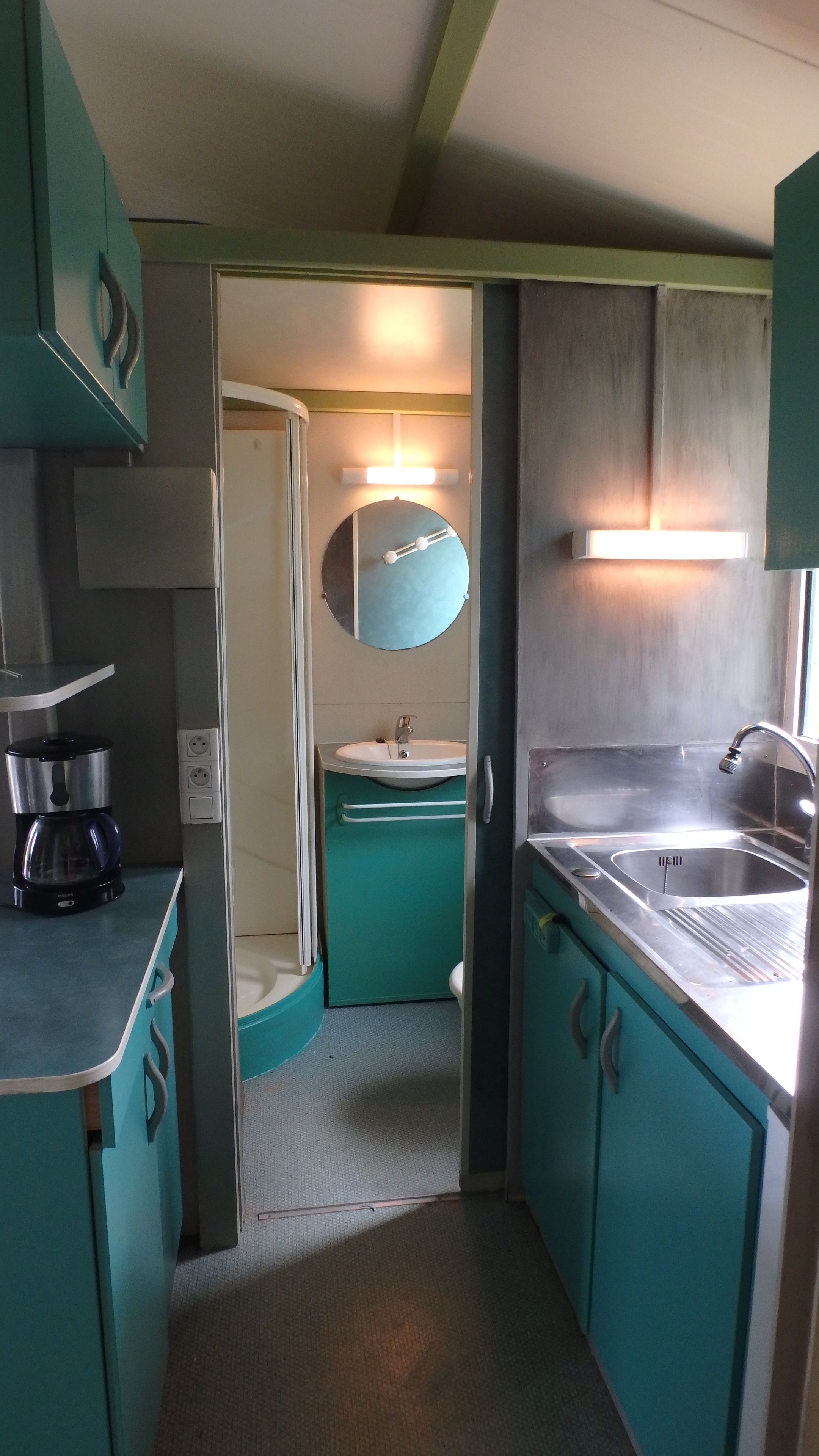 A compact kitchenette with a coffee maker, a sink, and a mirror.
