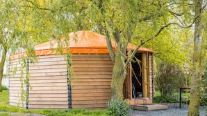 Eine Holzhütte mit geneigtem Dach, umgeben von üppiger Vegetation und Bäumen.