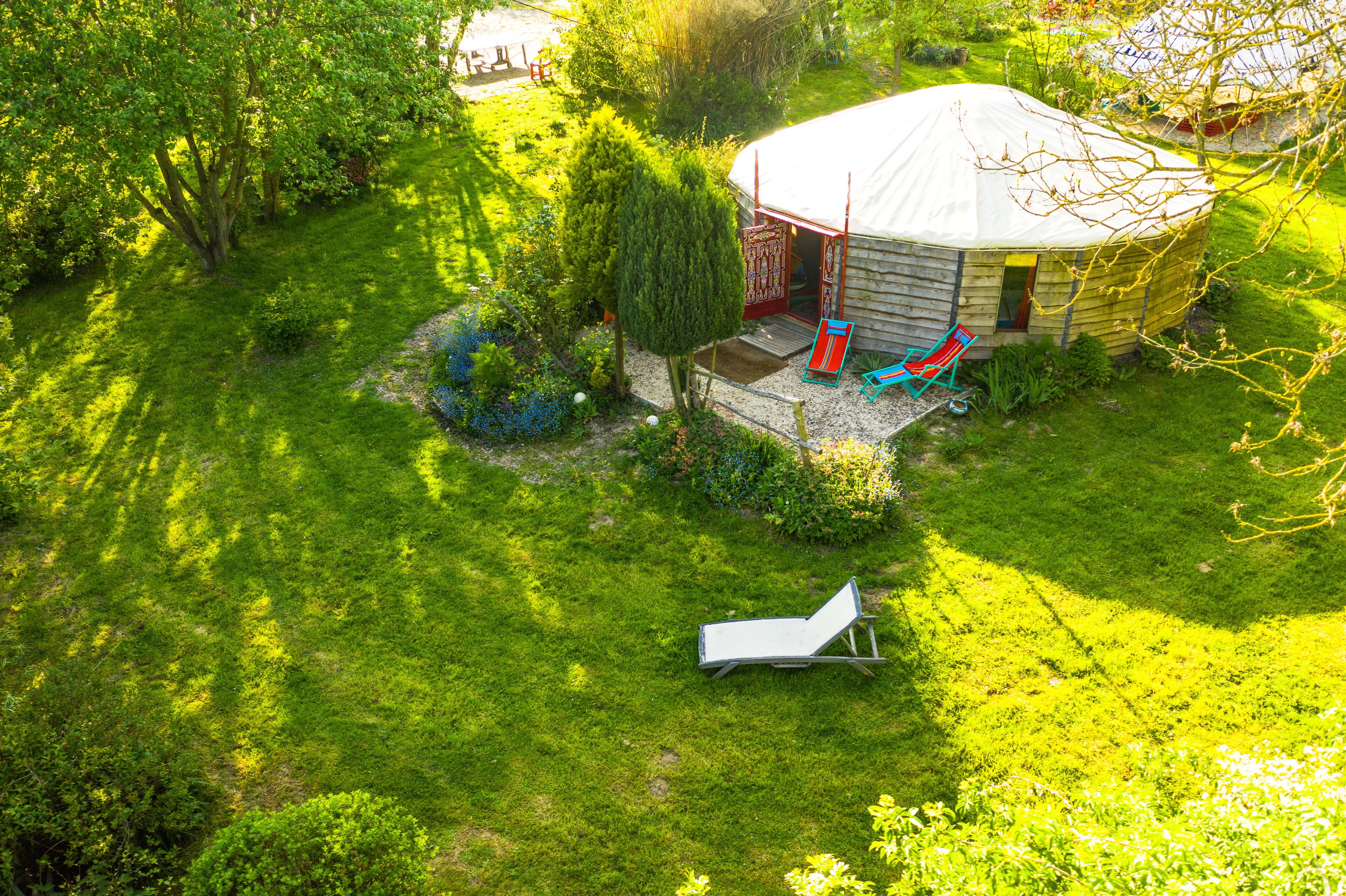 A yurt with a covered porch, surrounded by a lush garden and a grassy lawn.