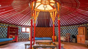 Ein traditionelles Jurten-Interieur mit einem zentralen Bett, Holzbanken und einer dekorativen Decke.