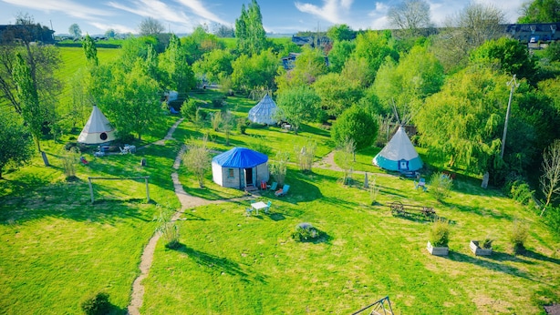 Ländliche Gegend mit mehreren Jurten und einem kleinen Haus, umgeben von grünen Feldern und Bäumen.