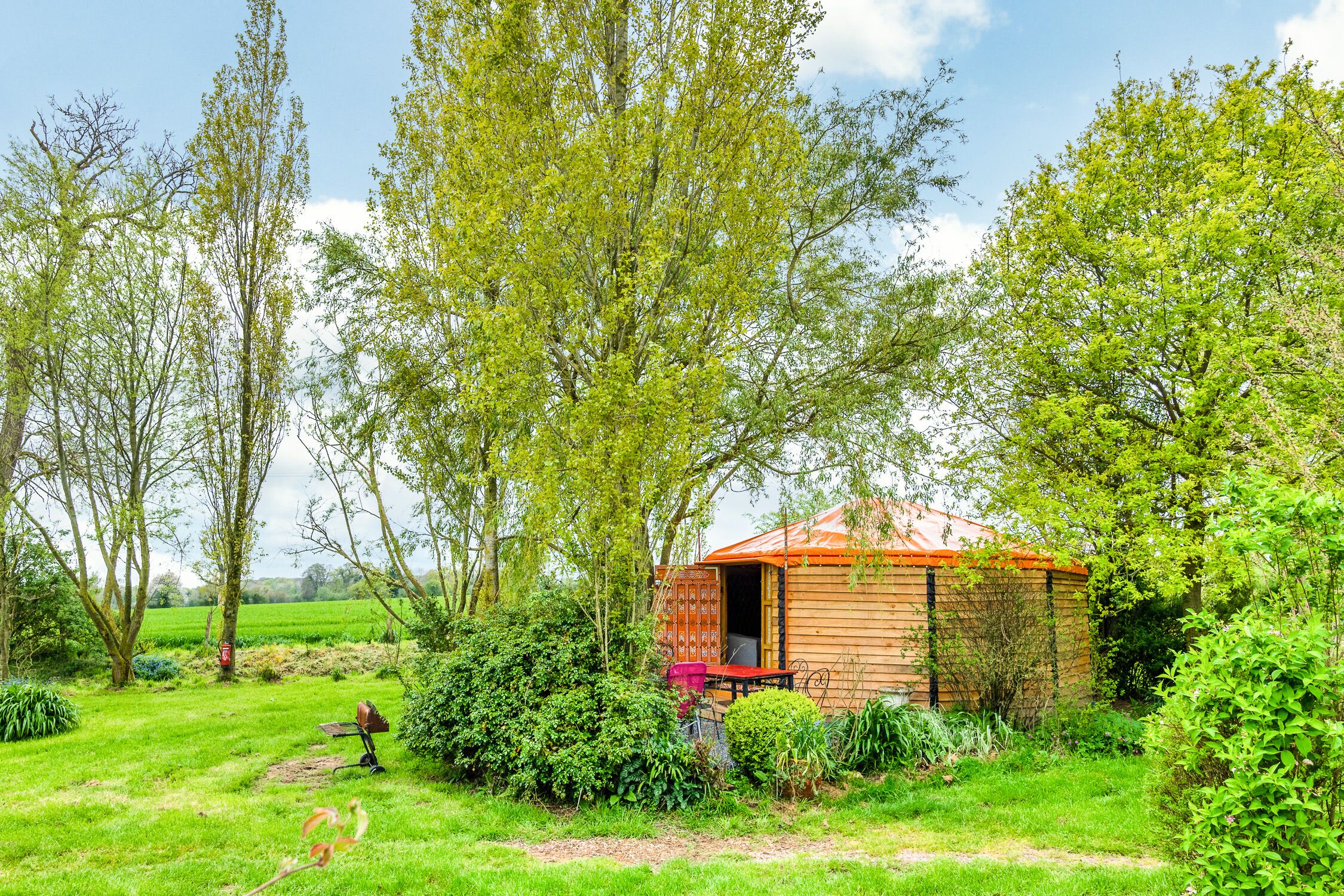 A rustic wooden cabin with a red roof, surrounded by lush greenery and trees.