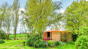 A rustic wooden cabin with a red roof, surrounded by lush greenery and trees.